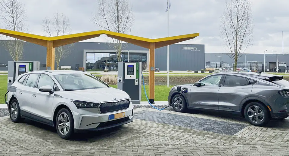 Two EVs charging at DC fast chargers in a modern business park with organized parking and green space